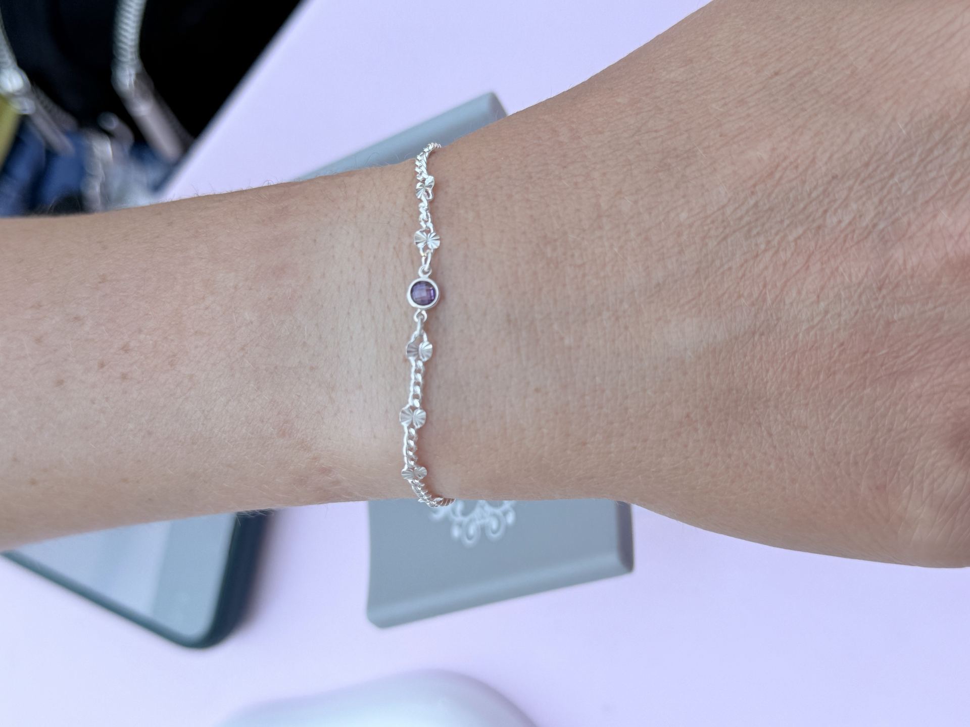 Silver bracelet with a bezel-set purple gemstone charm and textured link details, worn on a wrist