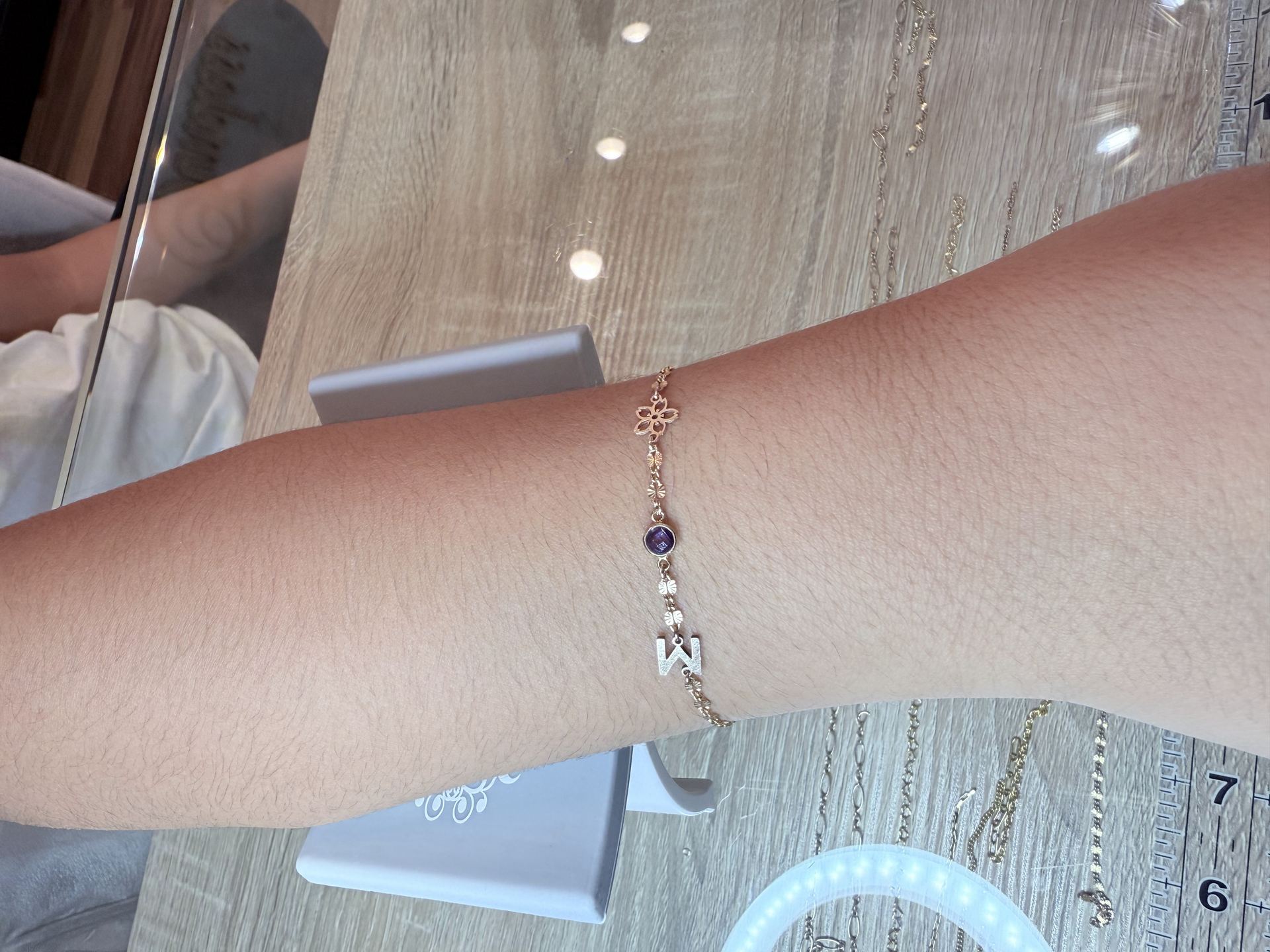Gold bracelet with an open flower charm, a round purple gemstone charm, and a letter charm reading M