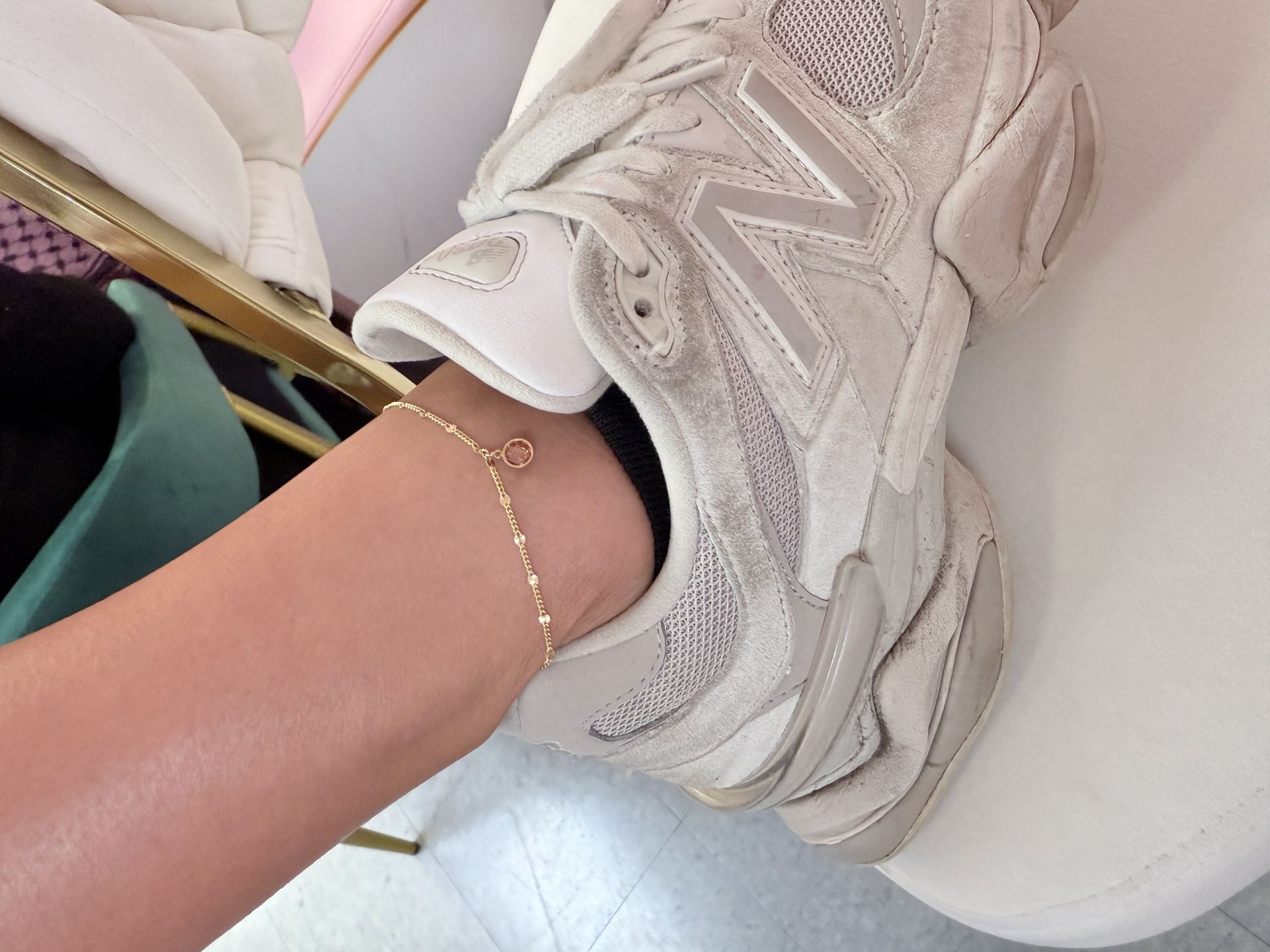 Gold beaded anklet with a round rose gemstone charm, worn above a sneaker