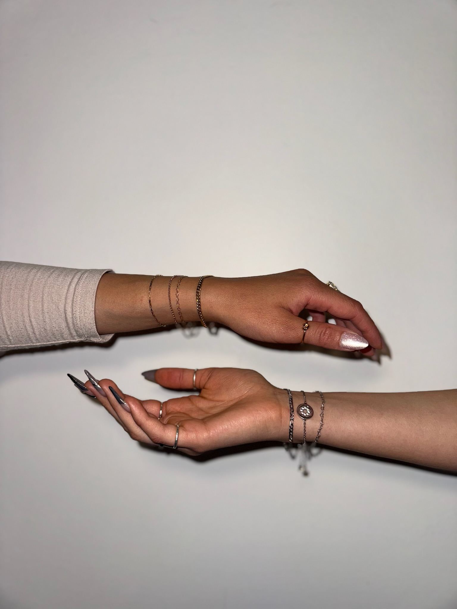 Two wrists layered with permanent jewelry bracelets against a plain background